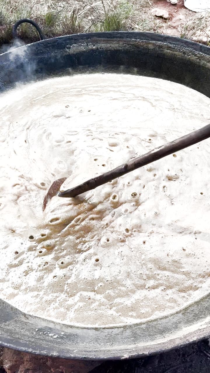 Cane juice reducing in an iron kadhai over wood fire, stirred by hand